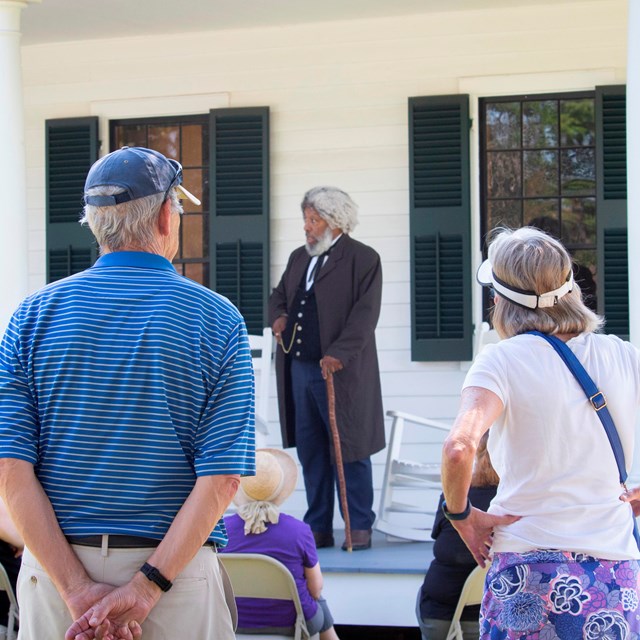 Two visitors watch a living history presentation of Frederick Douglass.