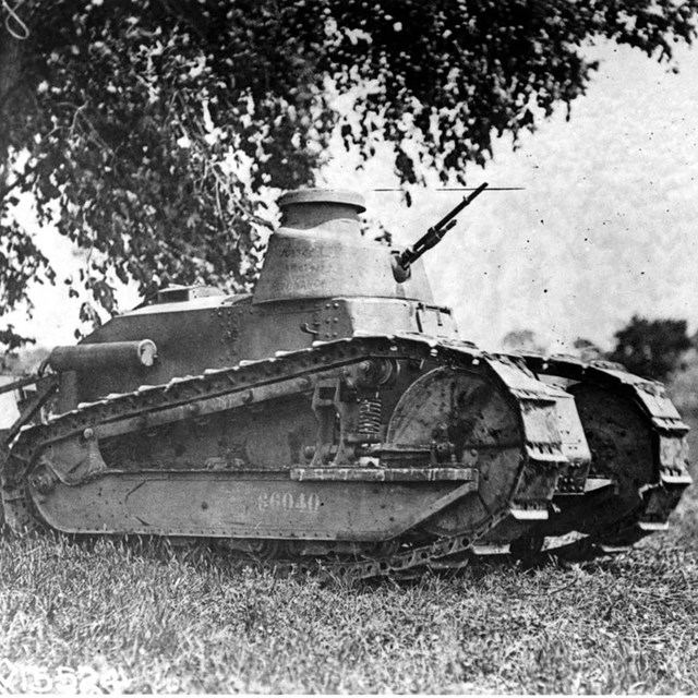 An army tank sits under a tree.