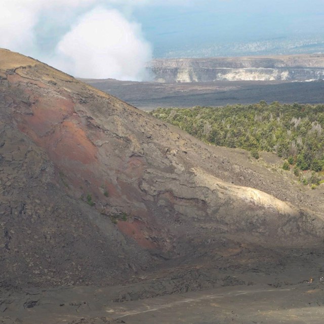 lava landscape in foreground with steam and greener hills in distance
