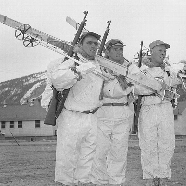 men pose in white suits with skis over their shoulders