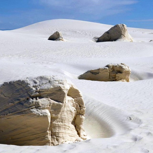 Rock in white sand dune with blue sky in distance