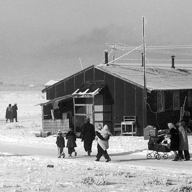 family walking in winter snow next to long low building on flat open plain