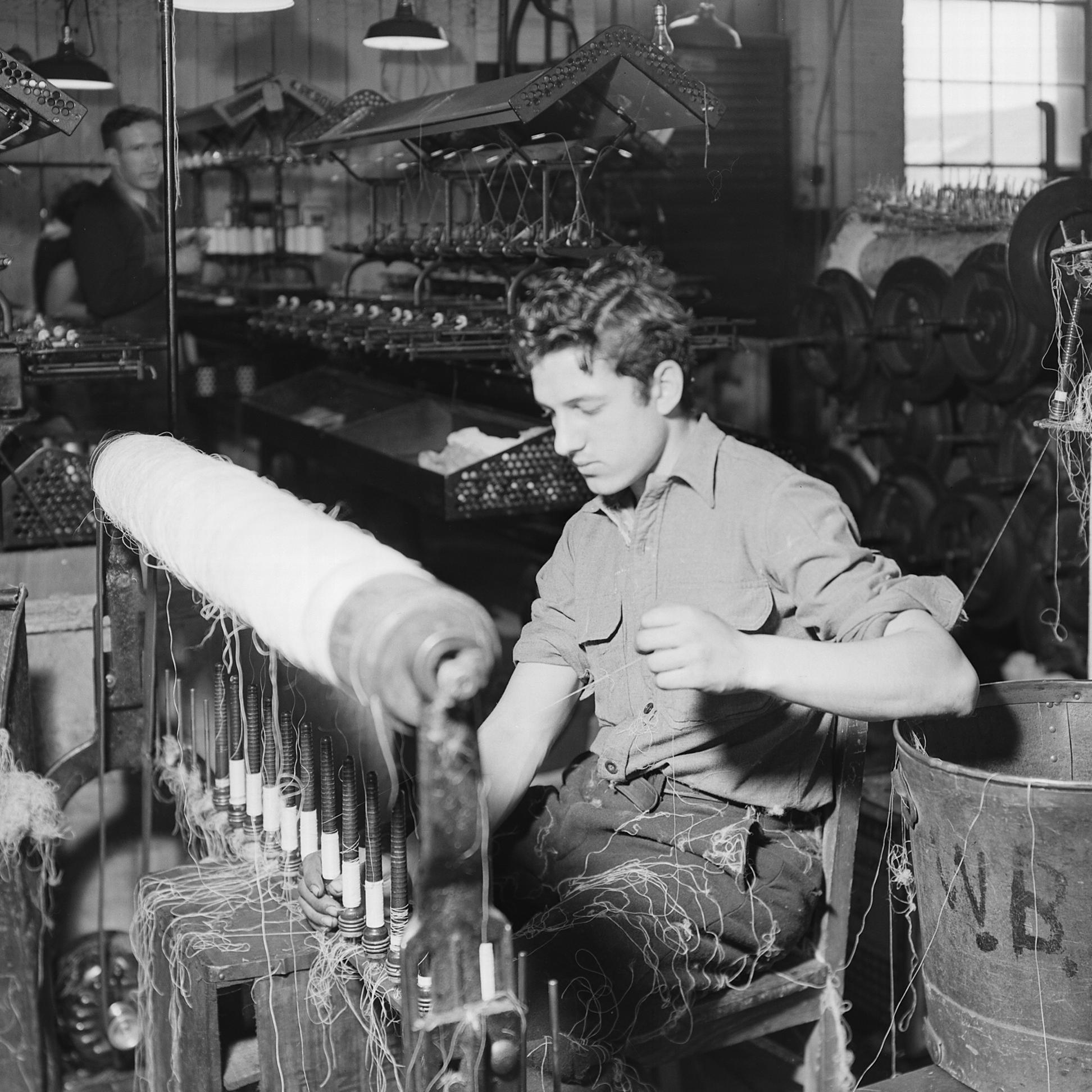 a man sitting and working at a silk weaving machine in a large factory 