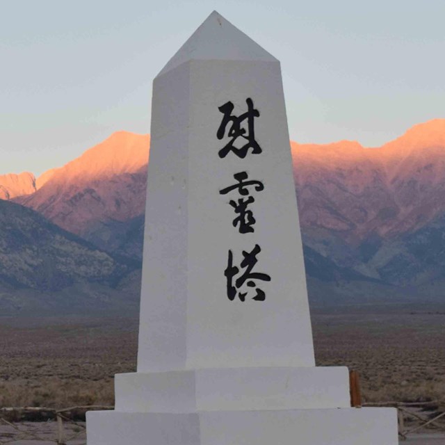 sunset next to a white monument with Japanese writing on it; mountains in background