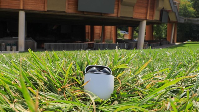 Headphone buds in a white case in the grass with theater in the background