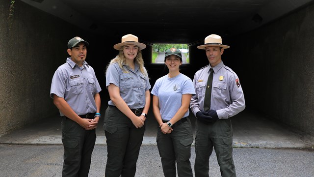 Two males and two females pose in different NPS uniforms