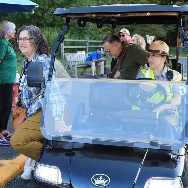 A ranger drops off patrons in a six passenger golf cart. 