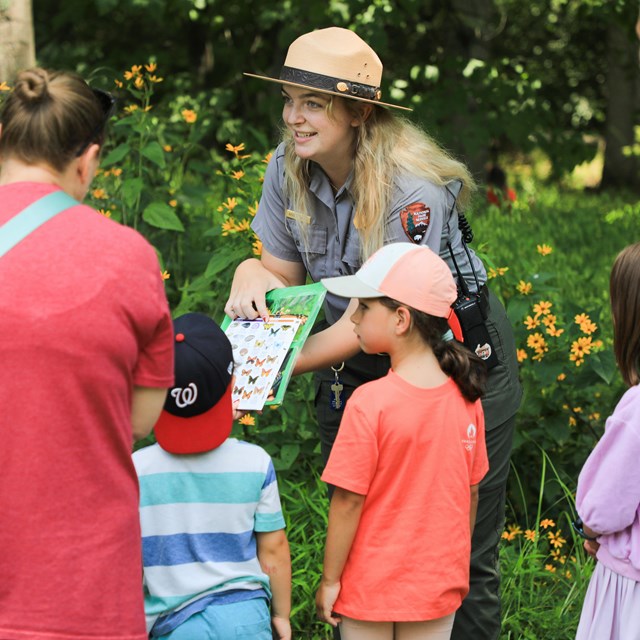 A ranger leads a program outside with a group of children accompanied by parents.