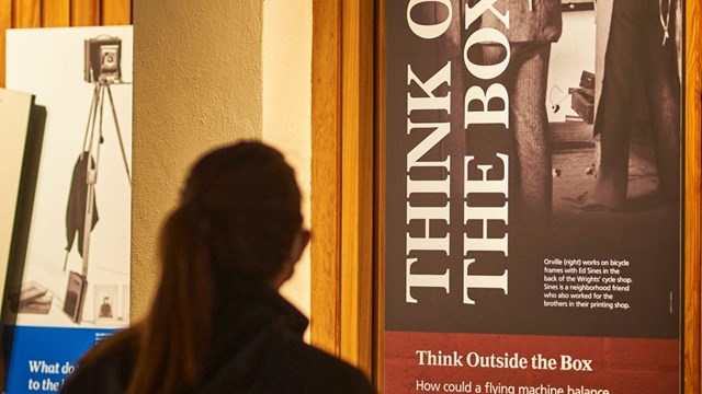 A woman standing and reading an exhibit labeled "Think Outside the Box"