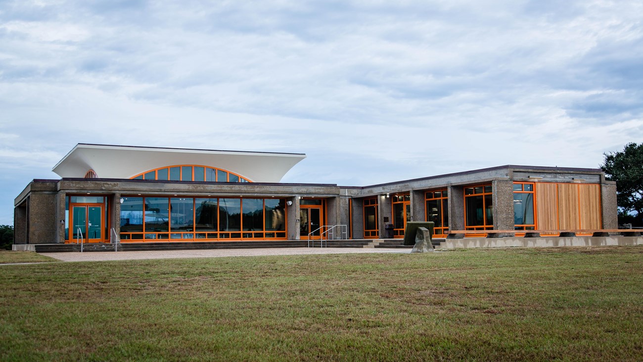 Rectangular building in short grassy field with blue, cloudy skies.