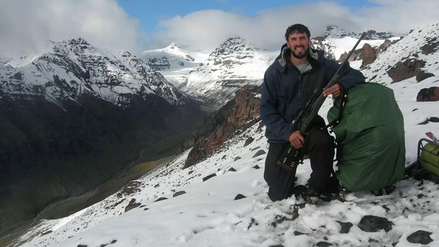 Man on mountain with hunting gear.