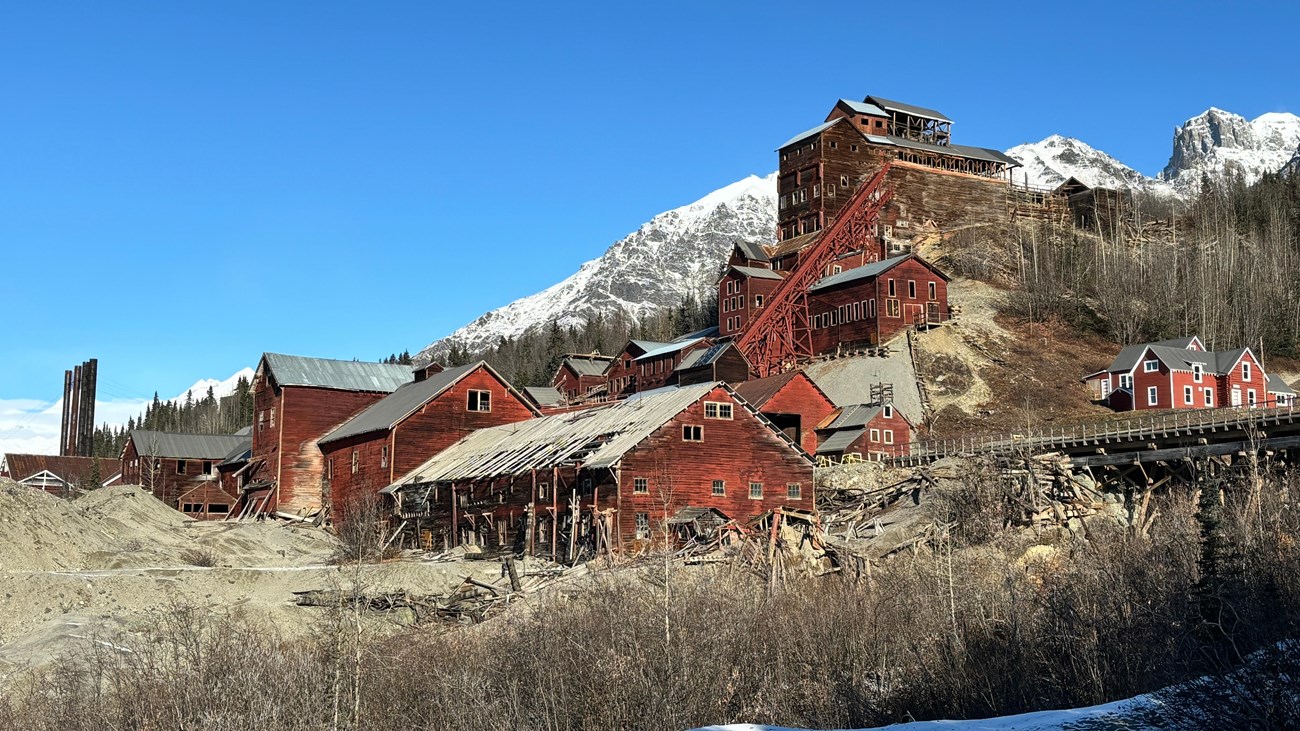 Large, red Kennecott Mill Building towers over other historic structures with a blue sky in the dist