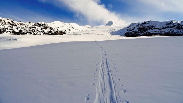 A figure treks through the snow in the distance.