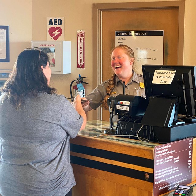 A visitor stands before a National Park Service Ranger and a fee station. 
