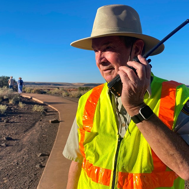 A volunteer in a yellow safety vest is speaking on a walkie talkie. 