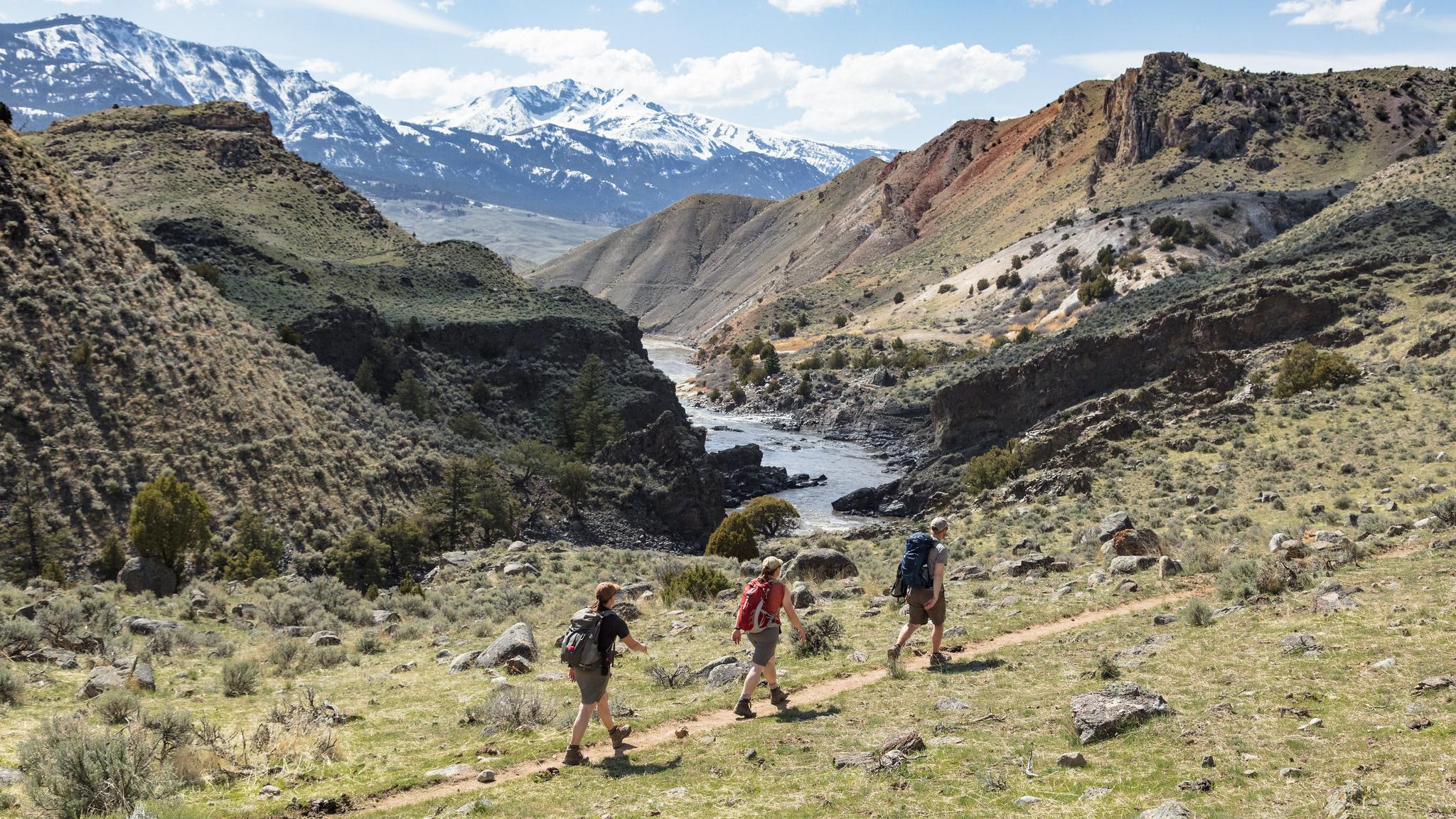 Hikers walking along a trail with river and mountain views.