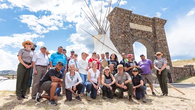 a group of people in front of a large, white teepee and stone archway