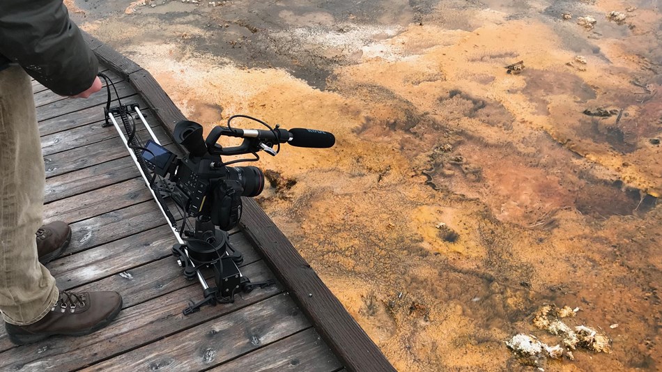 A camera mounted to a sliding apparatus resting on a wooden boardwalk.