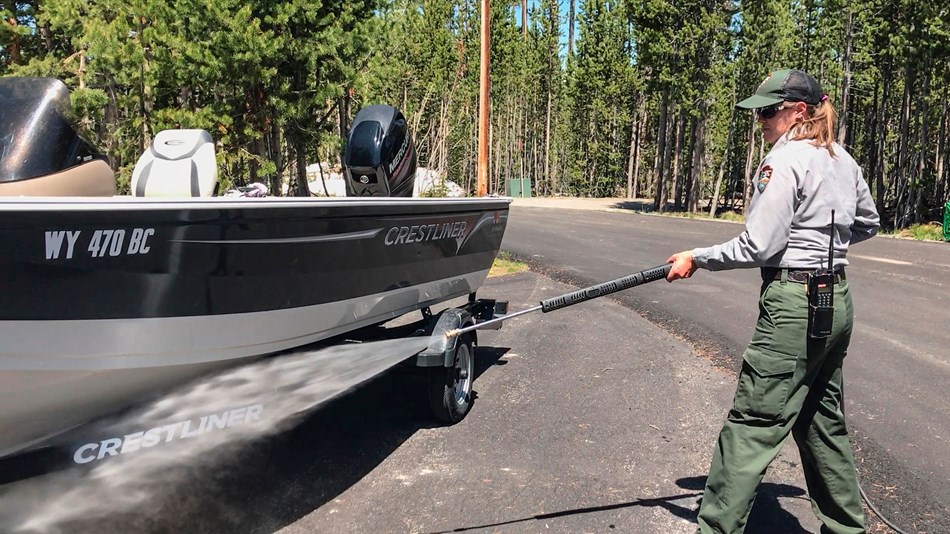 Photo of a park employee cleaning a boat with a power washer.