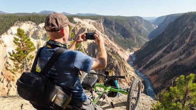 A person in a mobility chair photographs a canyon and river.