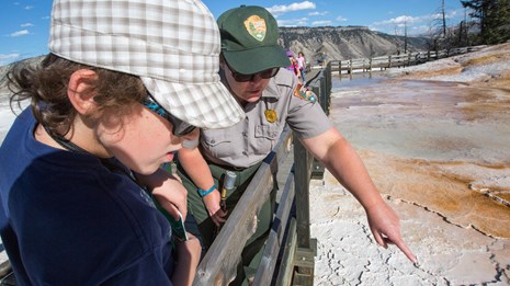 Interpretive ranger talks with a visitor while pointing out a hydrothermal feature.