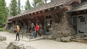 Three visitors leave the historic, one-story, stone and wood visitor center.