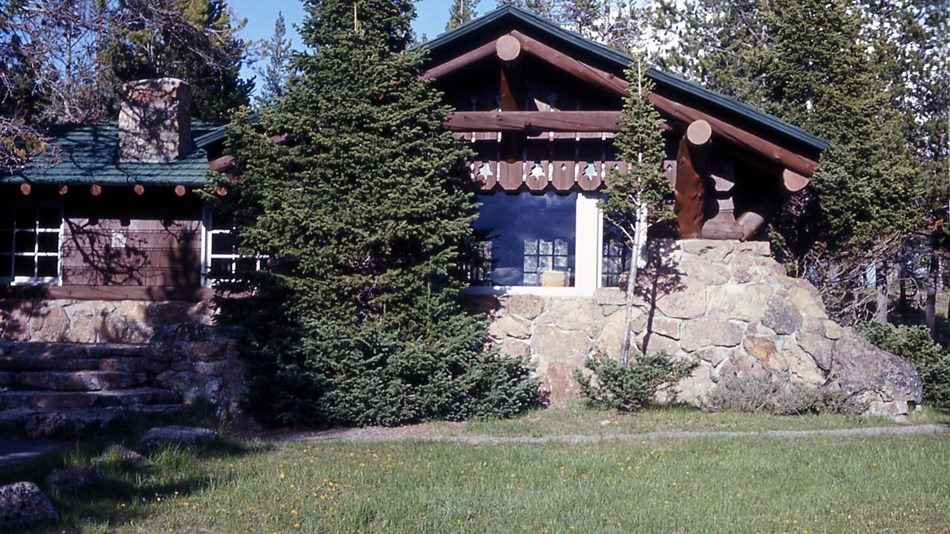 A stone and wood-log building sits amongst conifer trees.