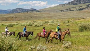 A line of horseback-riders travel across a sagebrush prairie.