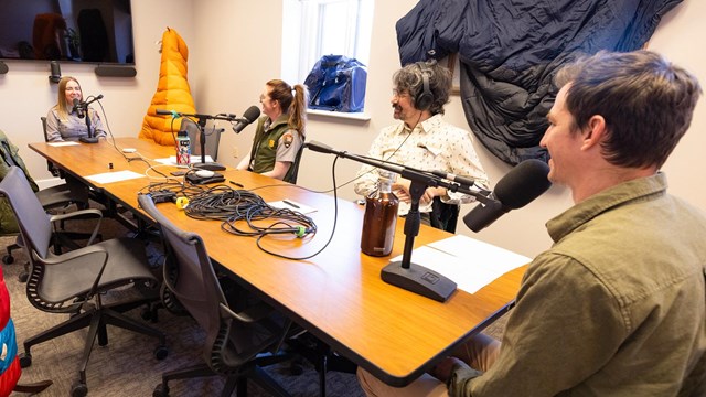 four park rangers talking into microphones around a conference table
