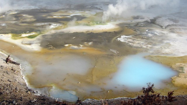 Multi-colored ground dotted with milky blue pools and rising steam.