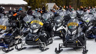 Snowmobiles parked in lines near a set of buildings.