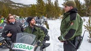 Visitors on a snowmobile talk with a park ranger