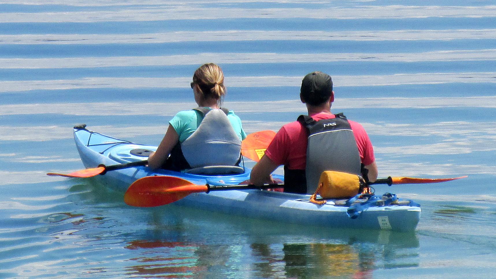 A couple paddles a two-person kayak across a still lake.