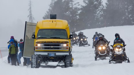 Snowmobiles and a snowcoach ride by a small group of bison