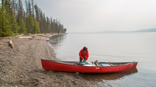 A person unloading a canoe on the shore of Yellowstone Lake.