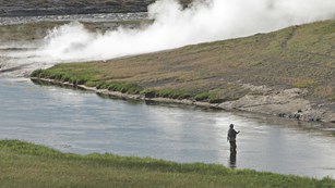 An angler standing in the water and fly-fishing during a misty day.