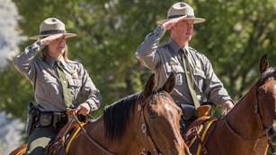 Two rangers on horseback salute during a ceremony.