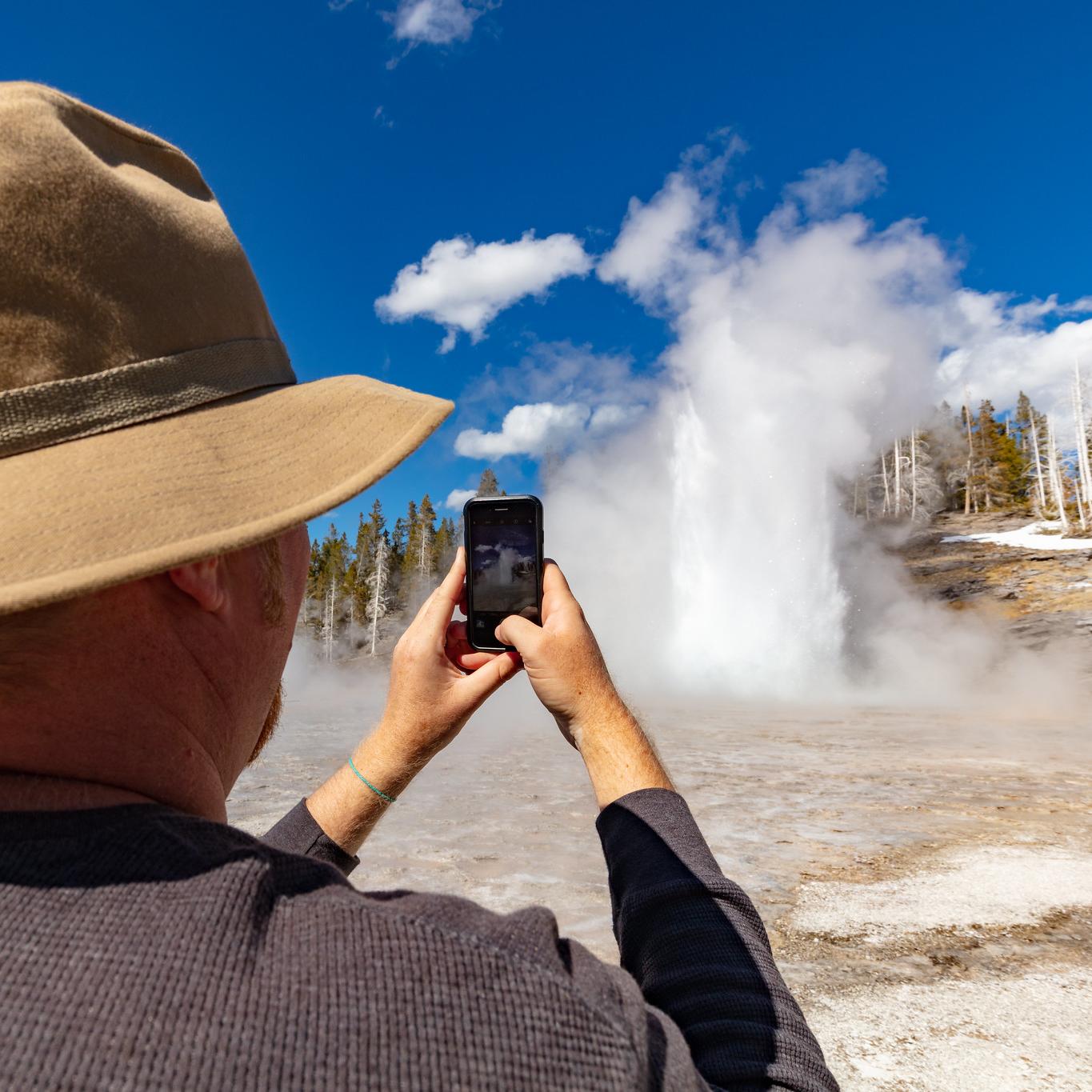 A person photographing the an eruption of a geyser