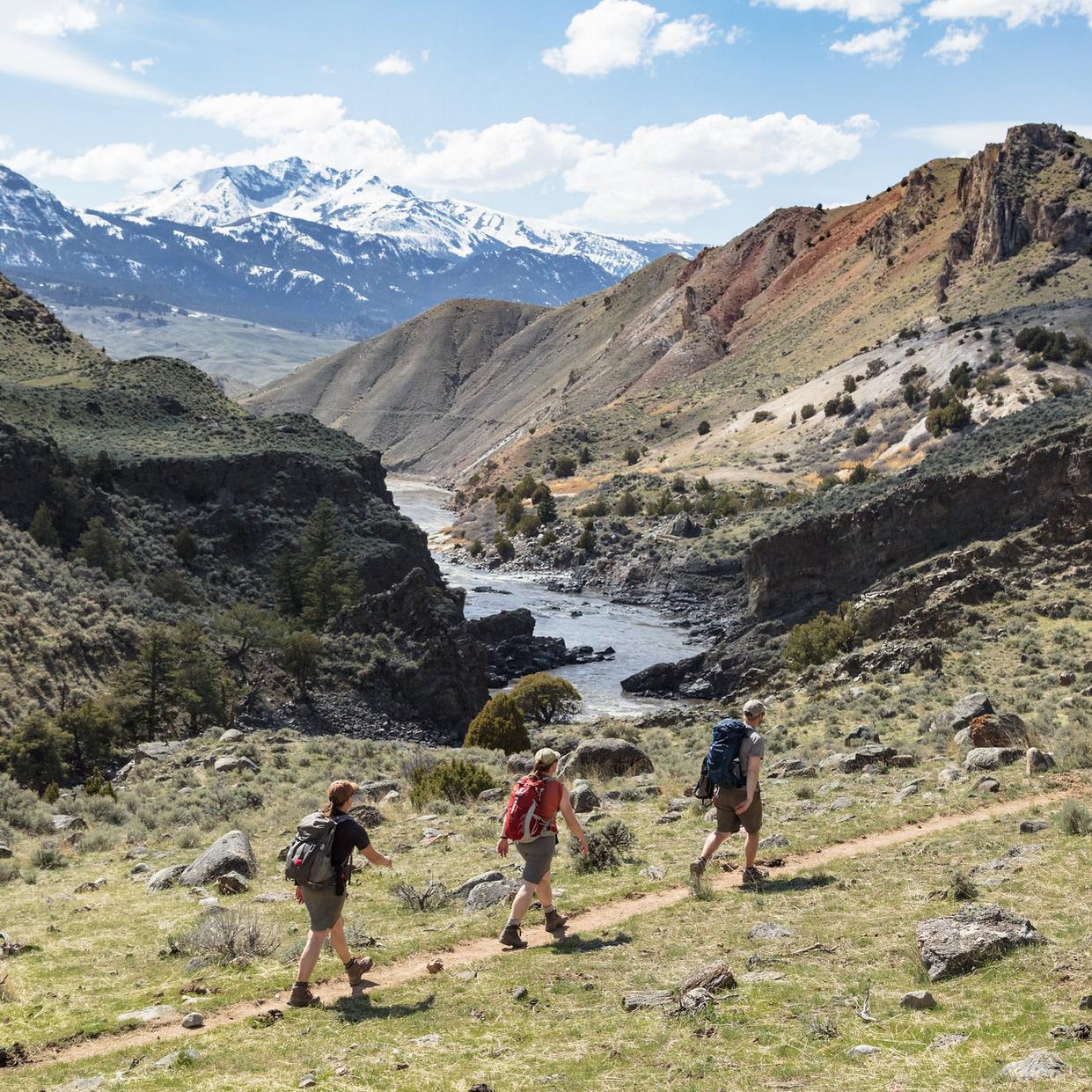 Hikers walking along a trail with river and mountain views.