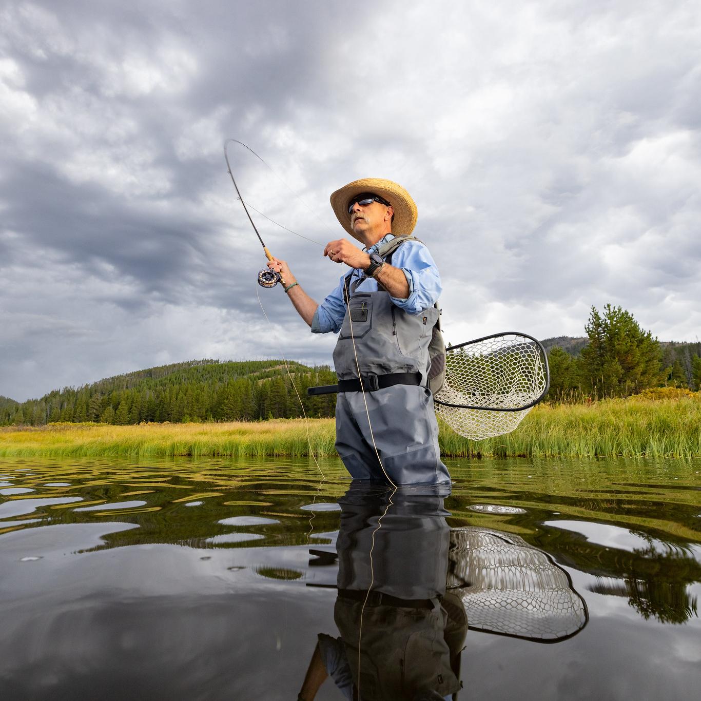 Angler fishing in a lake with a mountain in the background.