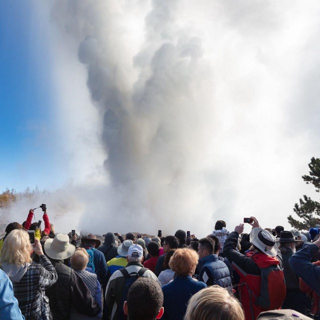 A large crowd of people watching a geyser erupt