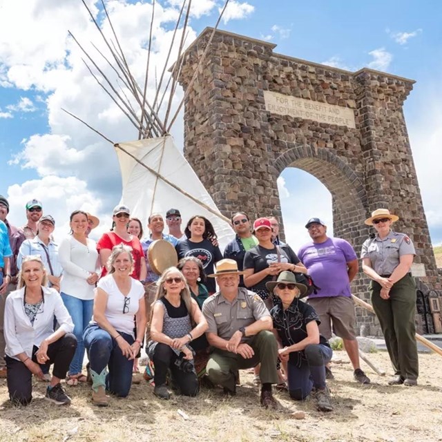 a group of people in front of a large, white teepee and stone archway