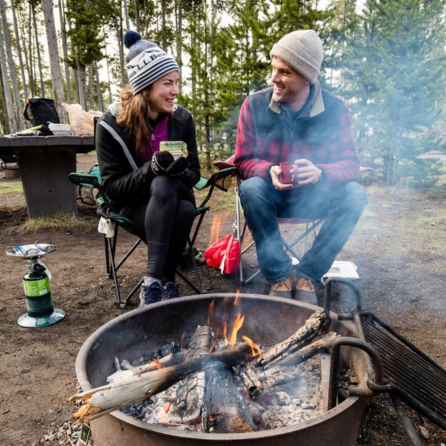 Two people sitting near a campfire on a chilly morning