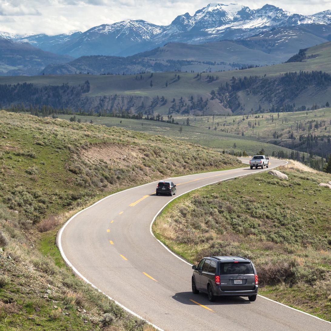 Cars drive through a winding road with mountains in the background.