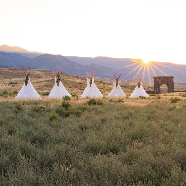 Row of teepees and stone arch at sunset