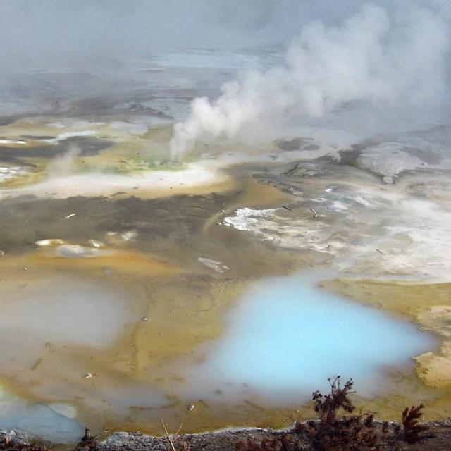 Multi-colored ground dotted with milky blue pools and rising steam.