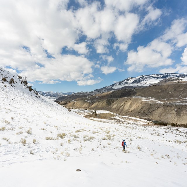 a person hiking through snow on a partly cloudy spring day