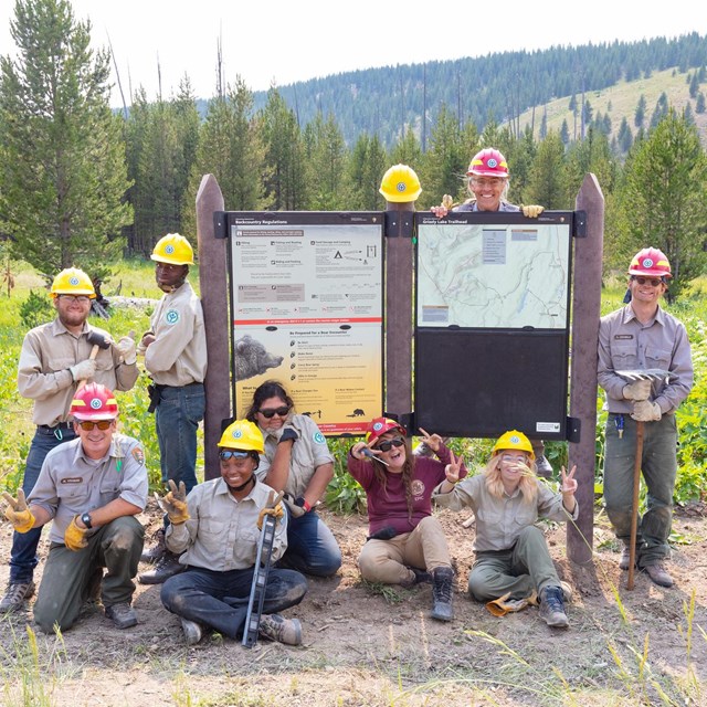 A group of teens and young adults posing next to a large trailhead sign they installed