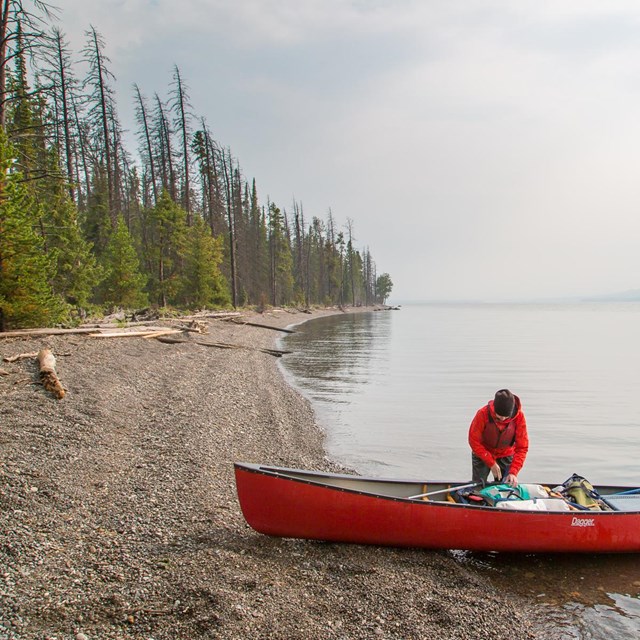 A person unloading a canoe on the shore of Yellowstone Lake.