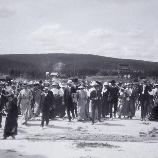 A historical photo of a group of people walking across a geyser runoff channel.